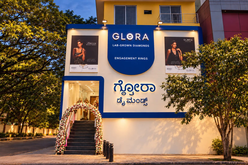 Evening front-facade render of Glora Diamonds showroom on Dickenson Road, Bengaluru, with illuminated signage and flower-decorated entrance