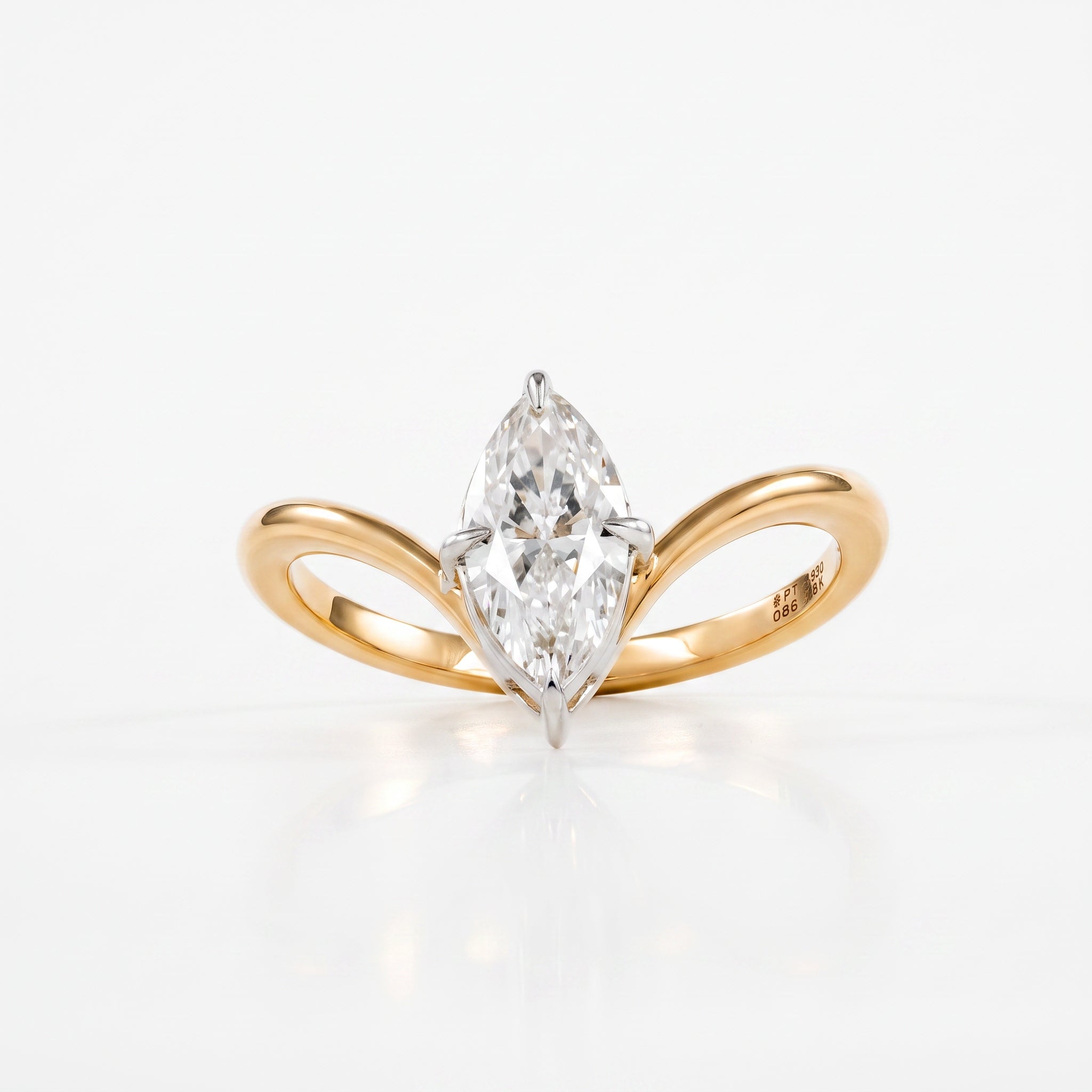 A yellow gold ring with a curved, double-bar design holding a marquise-cut diamond in a prong setting, photographed on a clean white background with a soft reflection.
