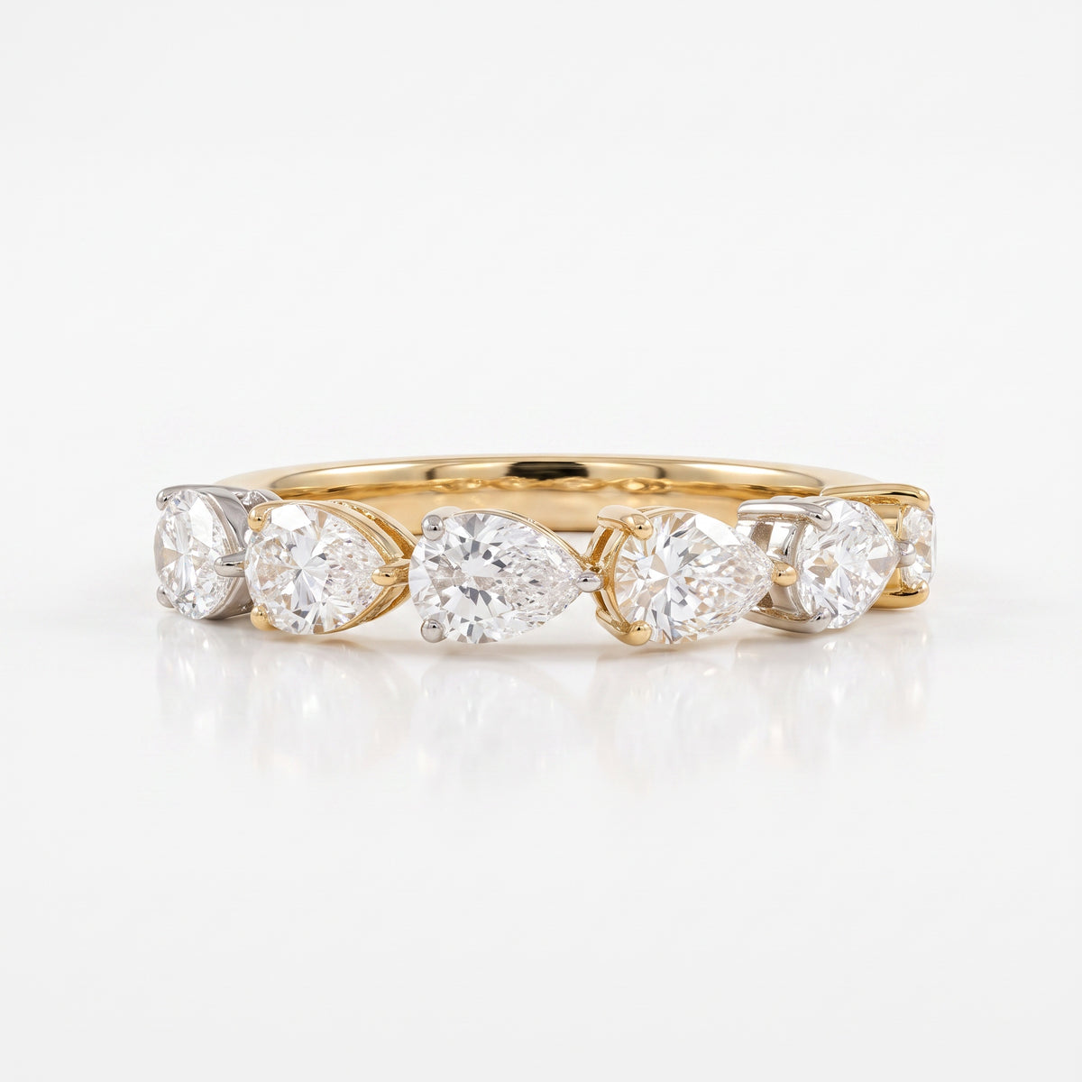 A yellow gold diamond band ring featuring five pear-cut diamonds in a row, set in a yellow gold band with silver-colored prongs, on a clean white background with a soft reflection.