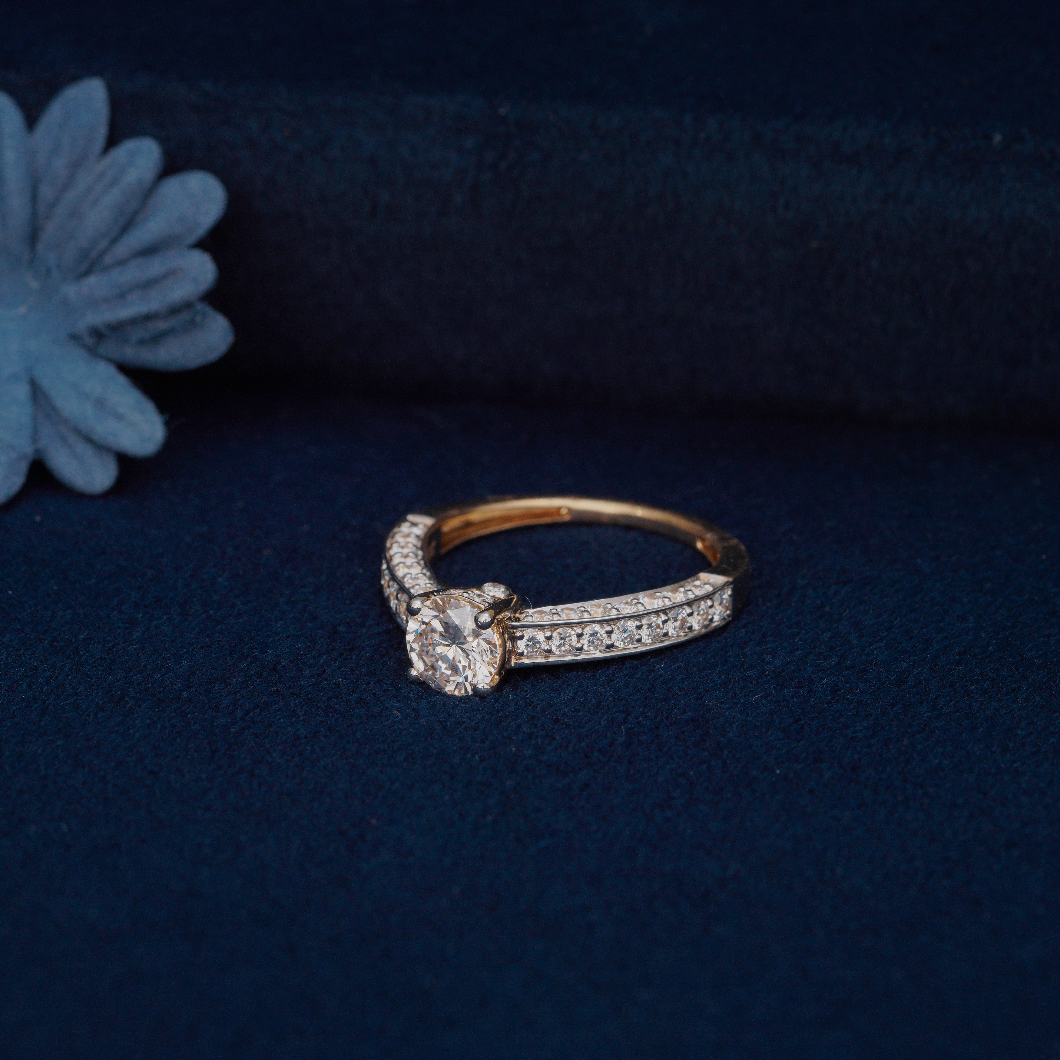 Stellar Solitaire Diamond Ring featuring a round brilliant-cut center stone and pavé-set diamond band in 18k yellow gold, displayed on a navy blue velvet background.