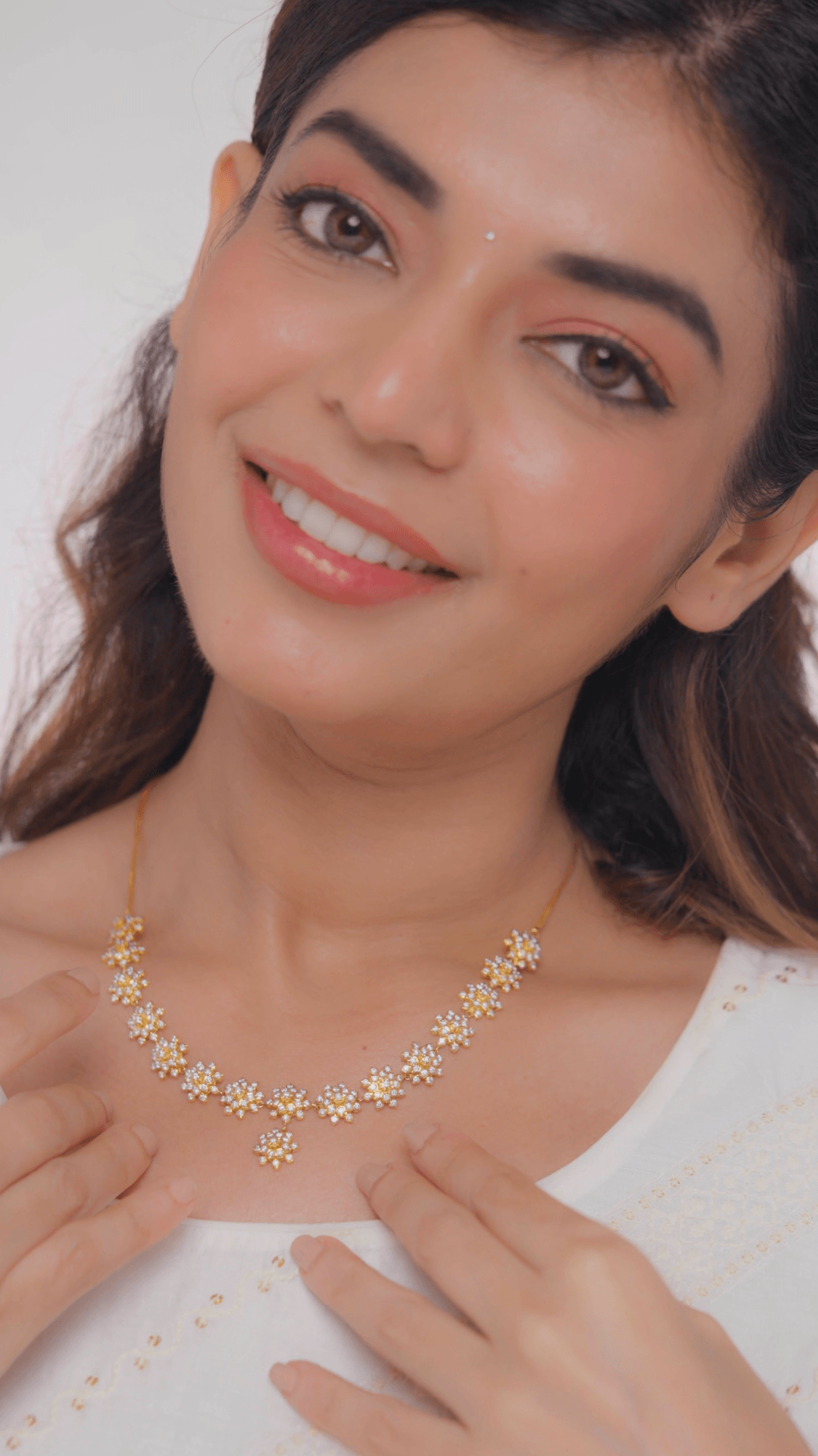 A woman smiling and showcasing a gold necklace with diamond accents.