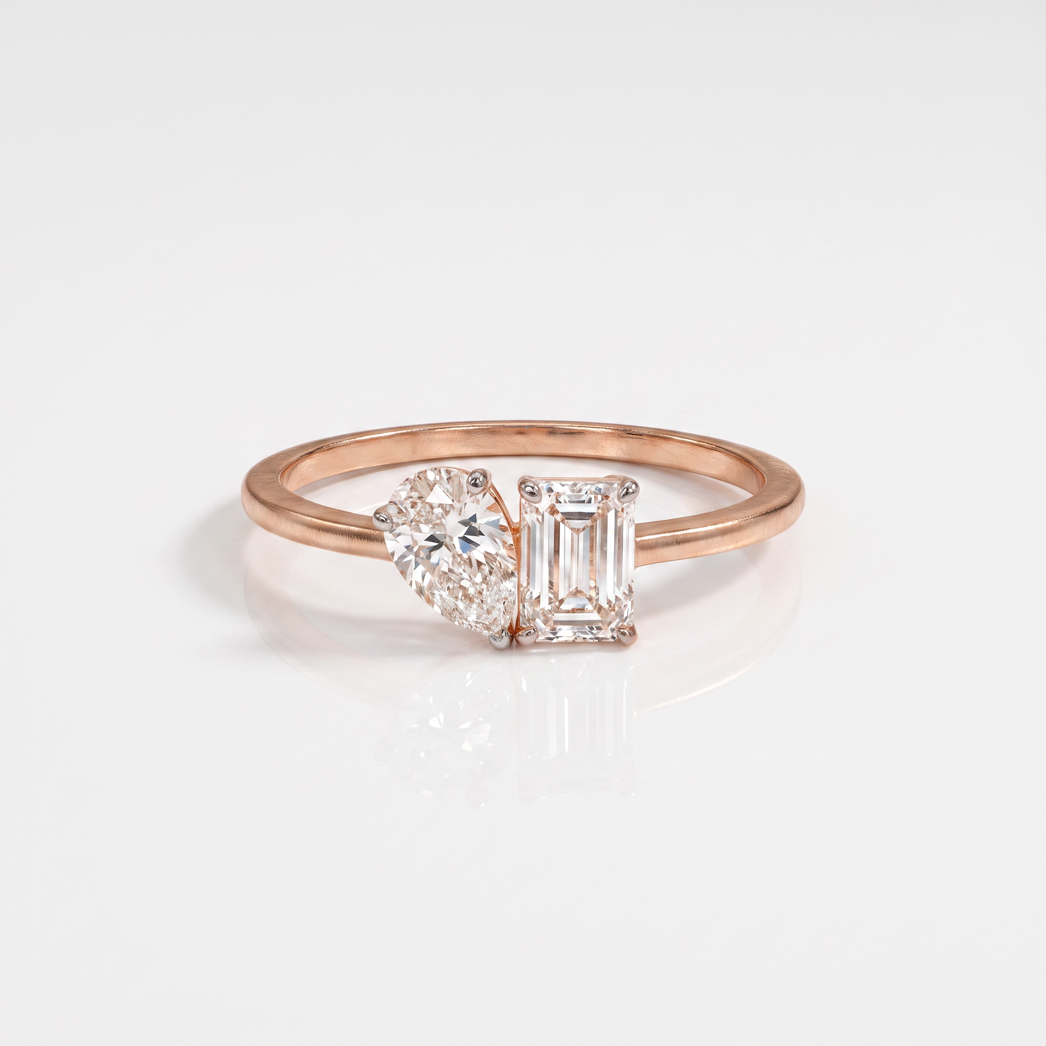 A rose gold ring with a split design featuring a pear-cut diamond on one side and an emerald-cut diamond on the other, set against a clean white background.