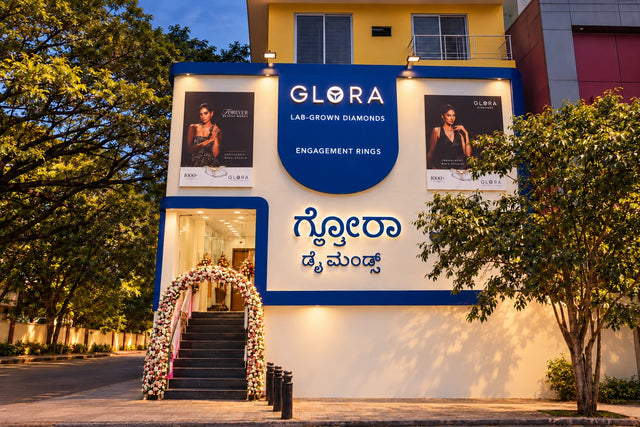 Evening front-facade render of Glora Diamonds showroom on Dickenson Road, Bengaluru, with illuminated signage and flower-decorated entrance