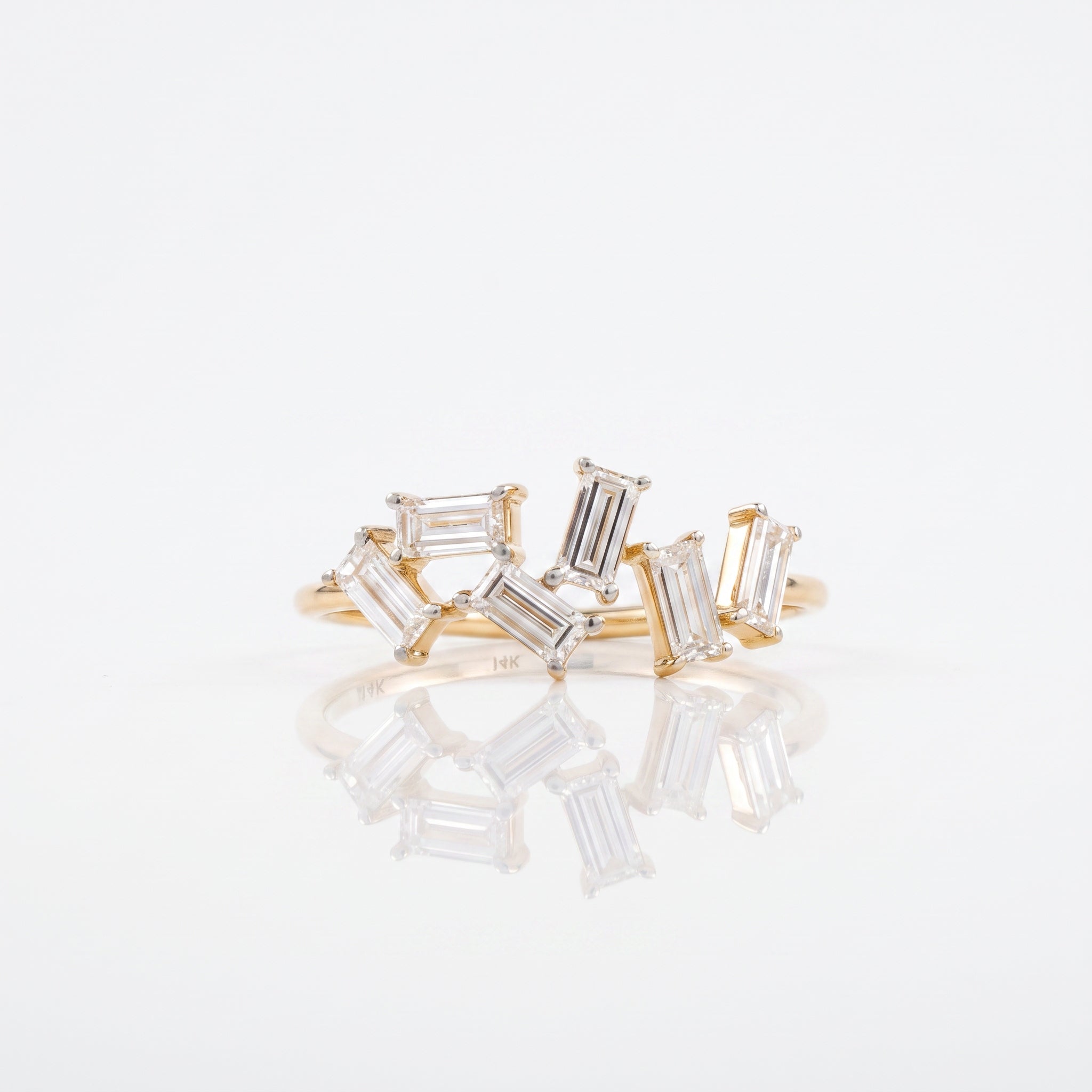 A gold ring featuring a cluster of baguette-cut clear gemstones in a prong setting, displayed on a clean white reflective surface.