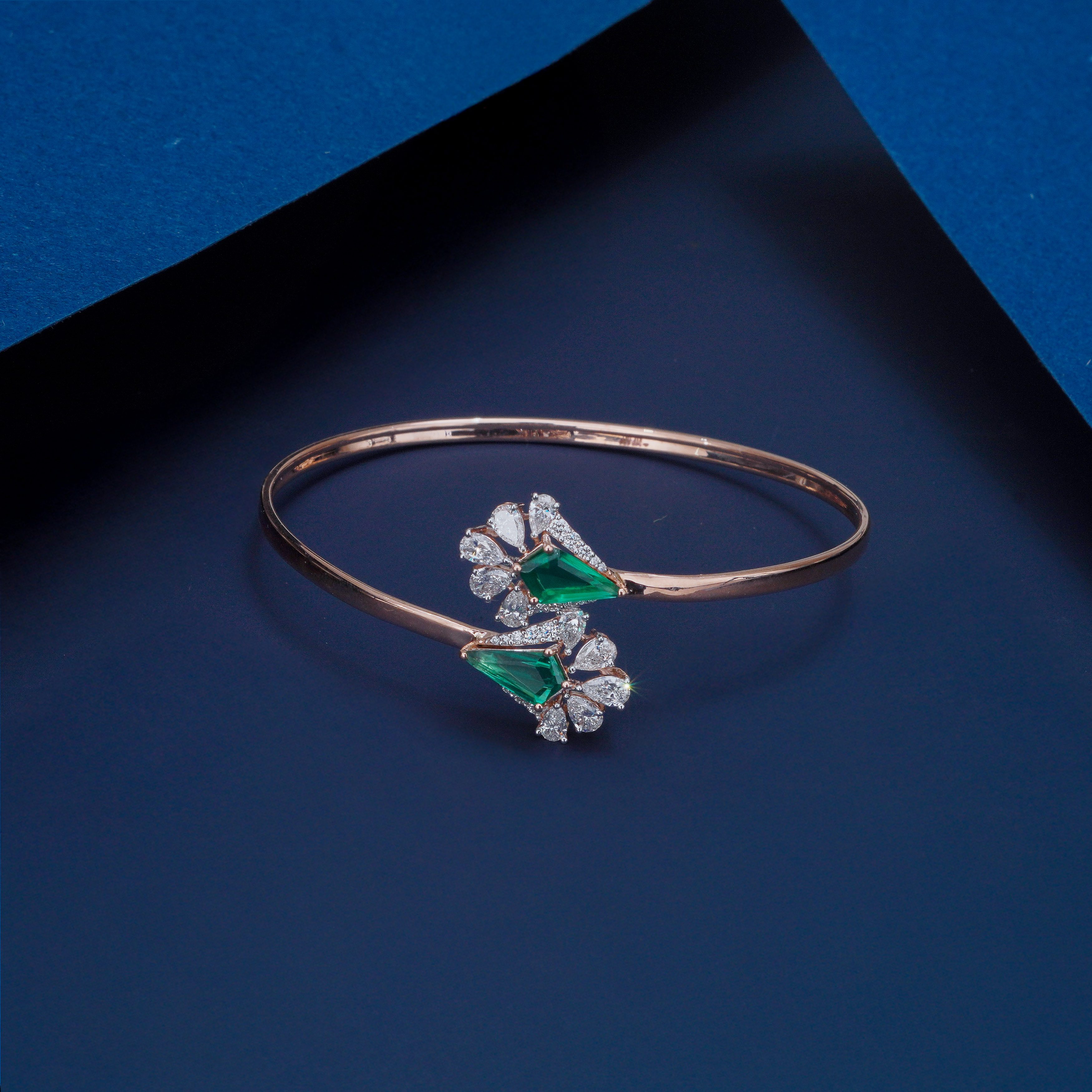 Rose gold bracelet with green gemstones on a blue background