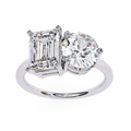 A silver-colored band diamond ring with one large round diamond and one large emerald-cut diamond side by side.