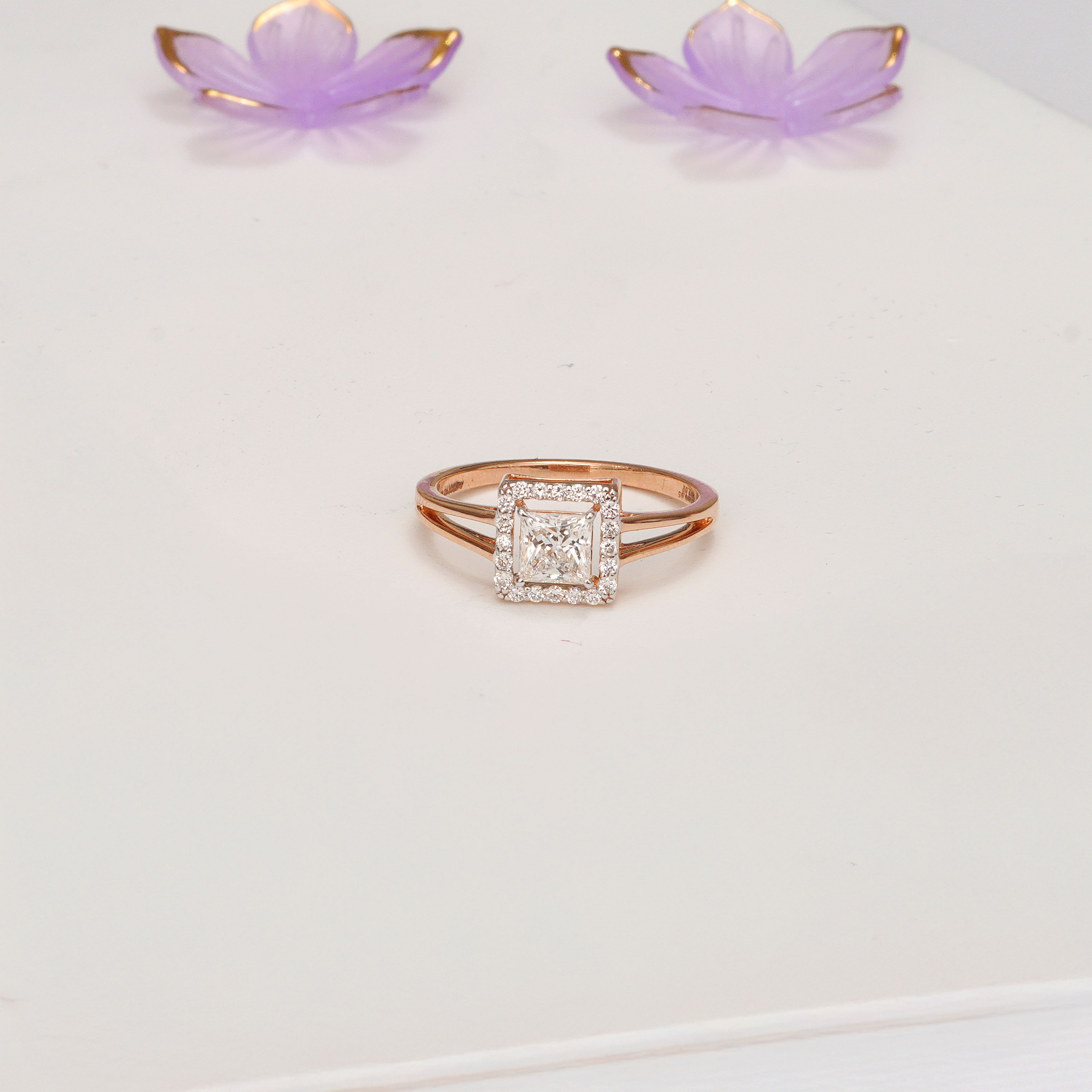 Rose gold ring with diamond on a white background. Princess cut lab diamond halo ring in 14k yellow gold with modern split shank band.