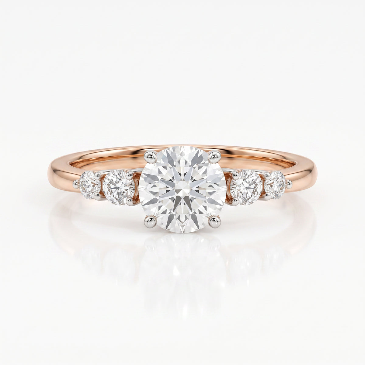 A rose gold engagement ring featuring a round brilliant-cut center diamond flanked by three smaller round diamonds on a clean white background with a soft reflection.
