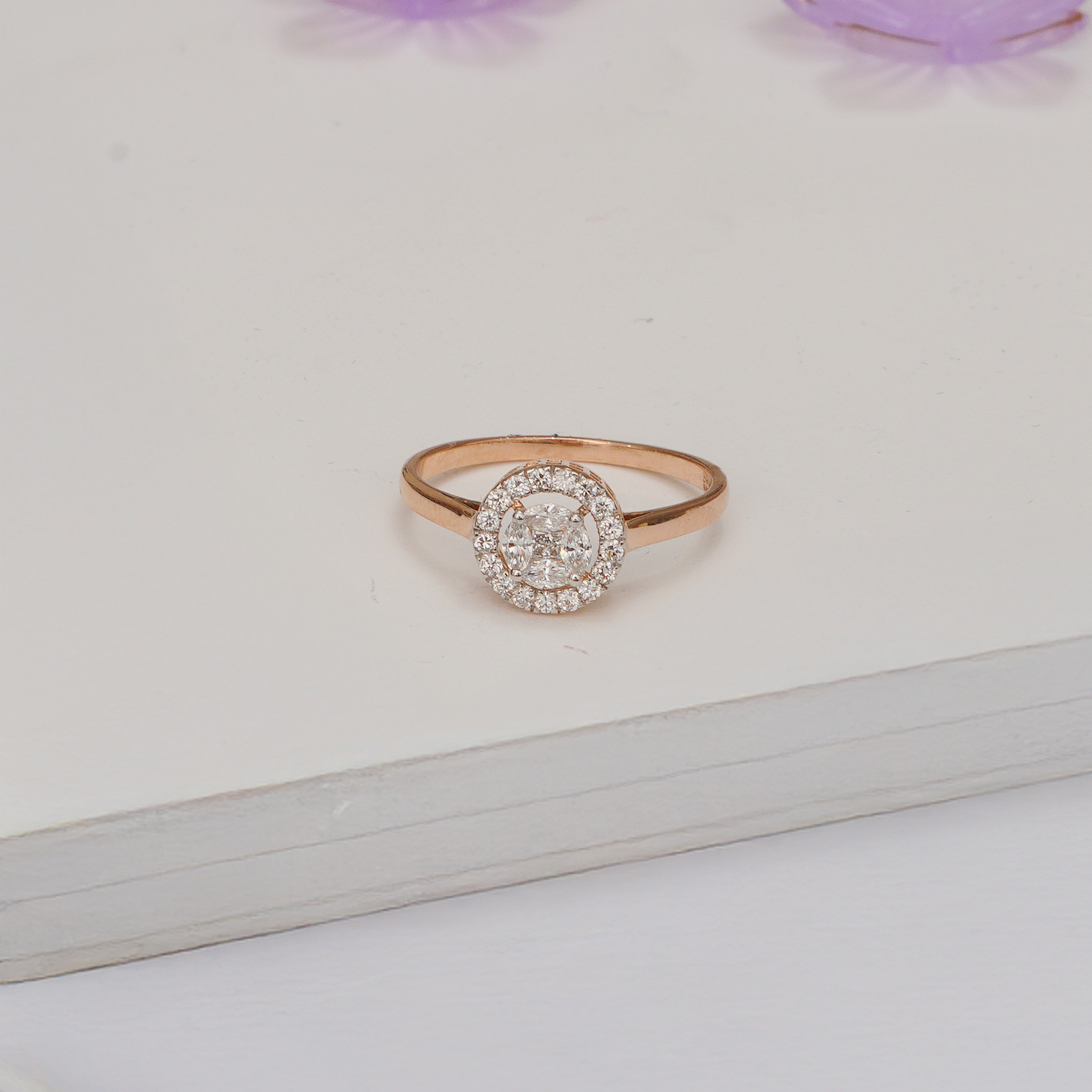 Rose gold ring with diamond cluster on a light background. Zola round cluster halo lab grown diamond ring in gold with sparkling halo design